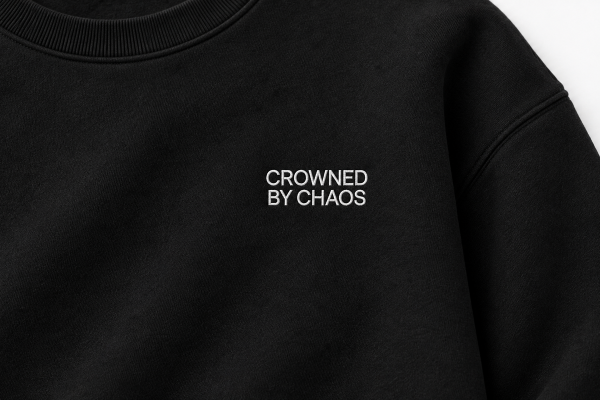 Détail du wordmark blanc CROWNED BY CHAOS sur le sweat-shirt noir