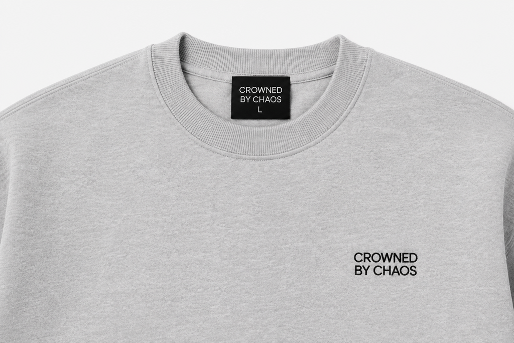 Détail du col côtelé et de l’étiquette CROWNED BY CHAOS du sweat-shirt gris chiné