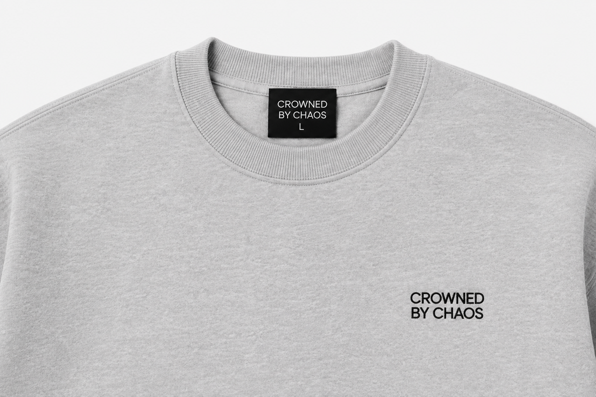 Détail du col côtelé et de l’étiquette CROWNED BY CHAOS du sweat-shirt gris chiné
