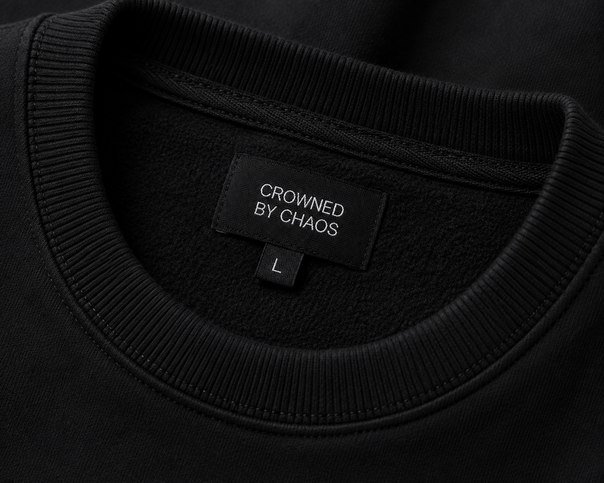 Détail du col côtelé et de l’étiquette CROWNED BY CHAOS du sweat-shirt noir