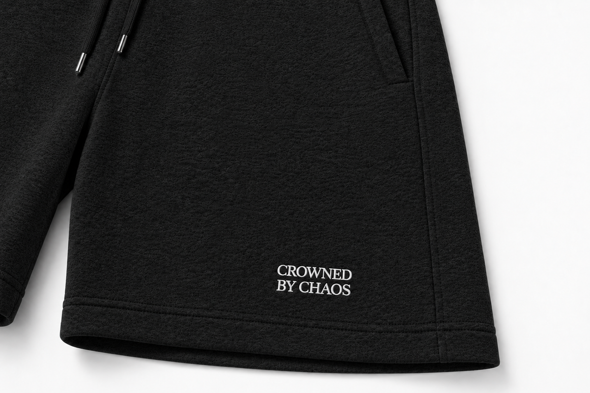 Détail du wordmark CROWNED BY CHAOS sur le short noir